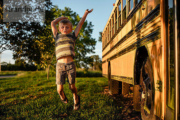 Kleines Kind springt vor Freude neben dem Schulbus  während es zurück zum Schulunterricht geht