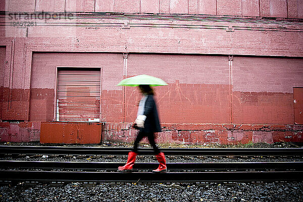 Eine Frau läuft im Regen über Eisenbahnschienen.