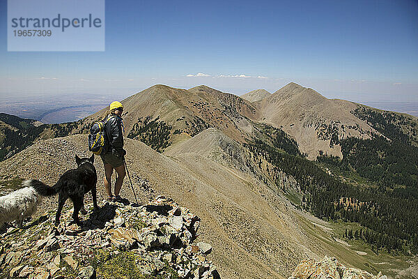 Frau steht mit zwei Hunden auf einem Bergrücken und blickt auf die Berge  La Sals  Utah.