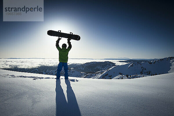 Eine männliche Snowboarder-Silhouette mit Blick auf Berge und Neuschnee.