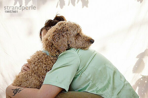 Woman and golden doodle share a hug outdoors