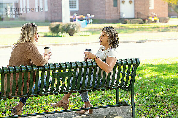 Zwei Frauen sitzen auf einer Bank  trinken Kaffee und unterhalten sich