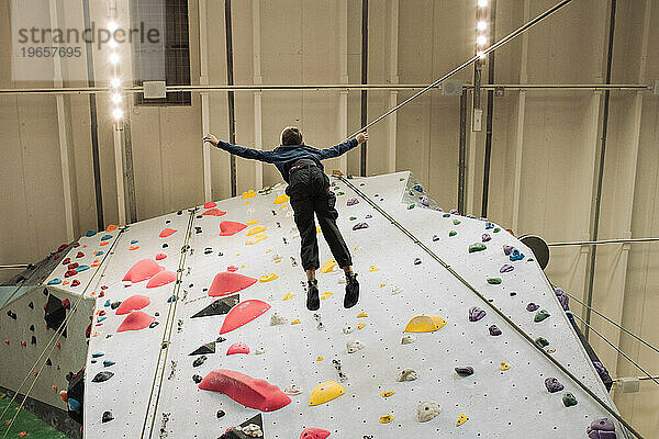 Junge liegt mit dem Rücken an einer Kletterwand  während er in einem Indoor-Fitnessstudio klettert