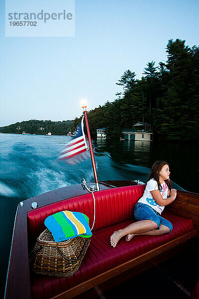 Ein junges Mädchen fährt nach Sonnenuntergang auf einem südlichen See auf dem Rücksitz eines antiken Holzbootes.