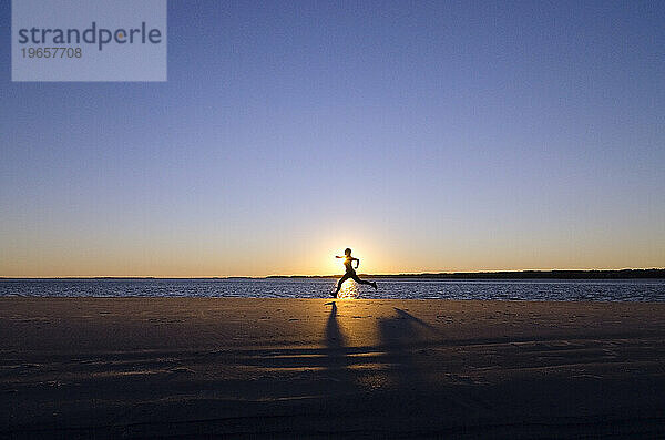 Die Silhouette einer jungen Frau  die kurz vor Sonnenuntergang am Strand von Hilton Head Island  SC  läuft.