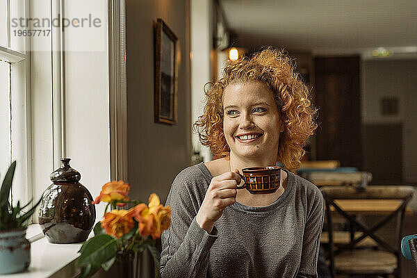 Fröhliche junge Frau sitzt am Tisch mit einer Tasse Kaffee im Café