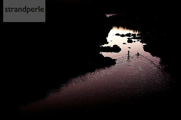 Silhouette eines Kajakfahrers und eines Stand-Up-Paddleboarders auf ruhigem Wasser bei Sonnenuntergang.