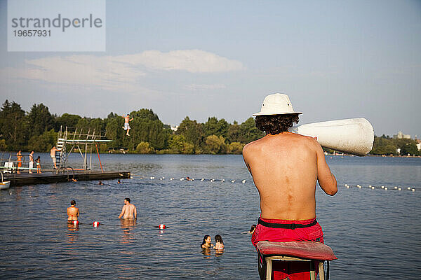 Ein Rettungsschwimmer wacht über Schwimmer  die vom Sprungbrett springen und in einem See schwimmen.