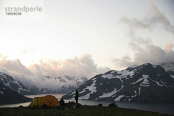 Zwei Männer genießen das letzte Licht des Tages vom Campingplatz in der Nähe eines Hochgebirgssees.