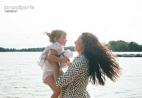 Mutter und Tochter lachen zusammen  während sie am Strand spielen