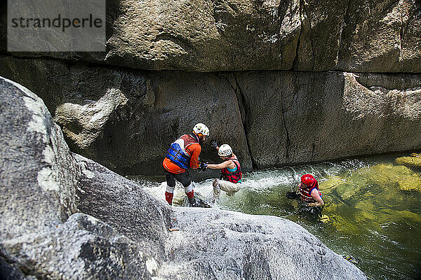 Während eines Abenteuers in Puerto Rico helfen sich drei Menschen gegenseitig beim Aufstieg auf einen Fluss.
