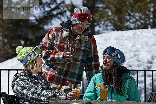 Drei Freunde trinken ein Bier auf der Außenterrasse eines Skigebiets.