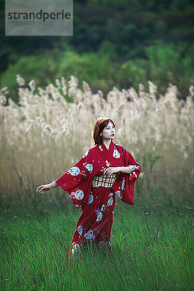 Mädchen im weißen Make-up-roten Kimono steht vor einem Hintergrund aus Schilf