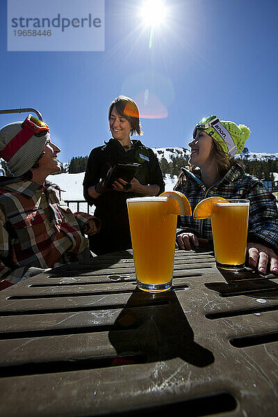 Junges Paar bestellt Essen und Bier auf der Außenterrasse eines Skigebiets.