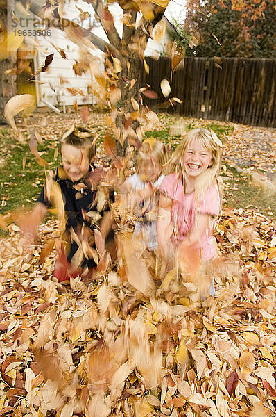 Drei Kinder  zwei Mädchen und ein Junge  spielen im Herbstlaub in Fort Collins  Colorado. (Bewegungsunschärfe)
