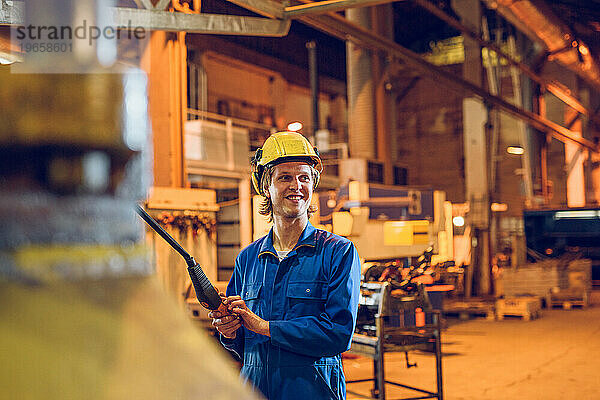 Lächelnder Mann  der in der Fabrik mit Maschinenbedienfeld arbeitet