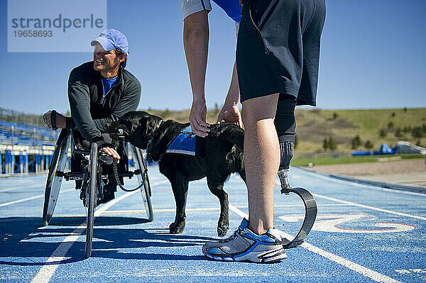 Ein Sportler mit seiner Laufprothese teilt einen Moment mit einem Rollstuhlsportler und seinem Arbeitshund.