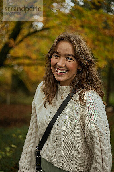 Junge Frau lacht und lächelt in Strickpullover im Wald