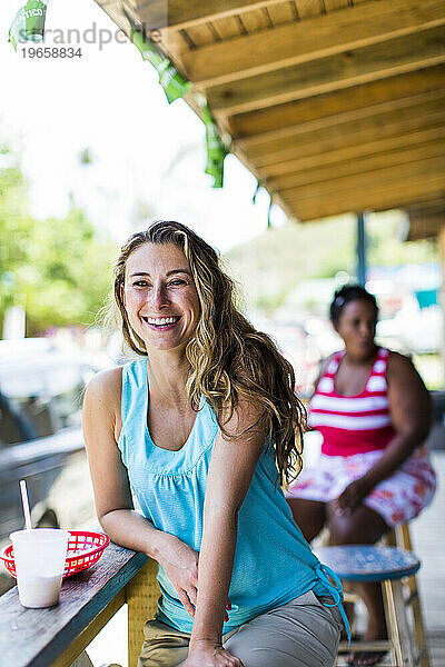 Eine junge Frau lacht  während sie auf einer Bank vor einer Bar in einem kleinen Dorf in Puerto Rico sitzt.
