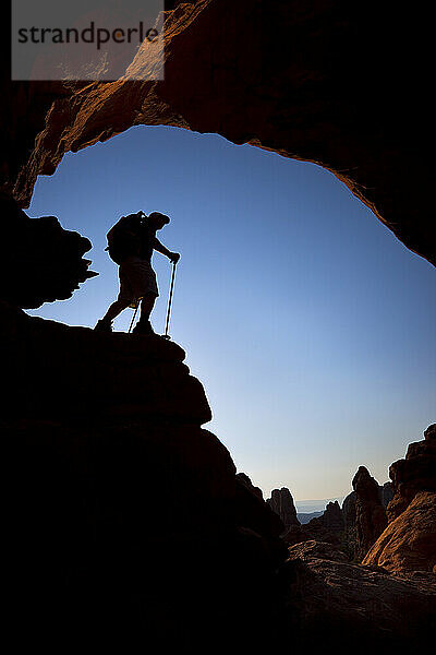 Silhouette eines Wanderers  der unter einem natürlichen Felsbogen im Arches-Nationalpark in Utah steht.