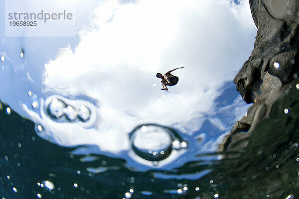 Unterwasserperspektive eines Mannes  der von einer Klippe ins Meer springt.