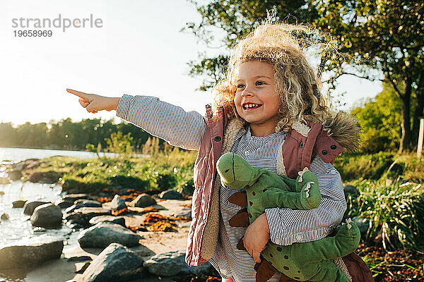 Kind hält seinen Dinosaurier und zeigt glücklich auf den Strand