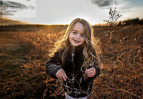Fröhliches junges Mädchen lächelt im Herbst im Blumenfeld