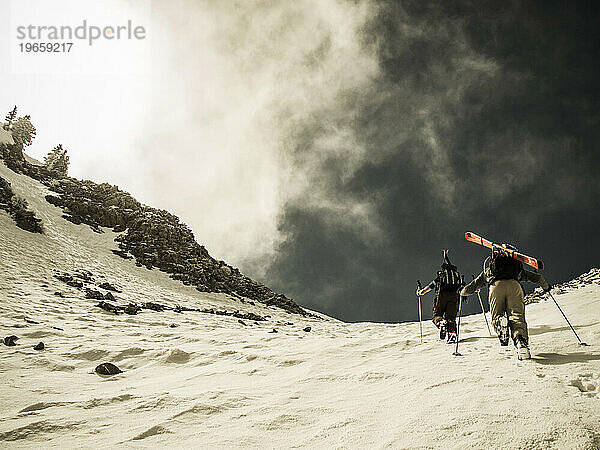 Zwei Personen wandern mit Skiausrüstung einen Schneehang hinauf.