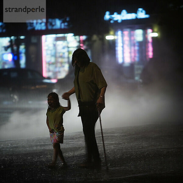 Eine Frau und ein Kind überqueren nachts die Straße.