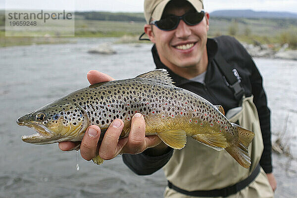 Man smiles while holding a fish in Montana.