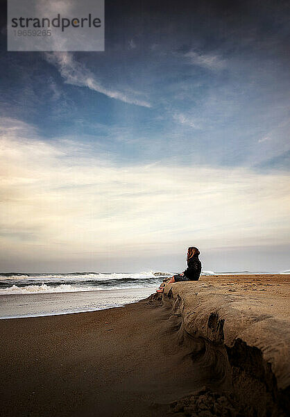 Junges Mädchen sitzt bei Sonnenuntergang ruhig am Strand