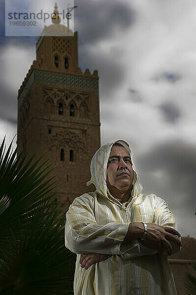 Ein Marokkaner steht in traditioneller nordafrikanischer Kleidung in der Nähe einer alten Moschee.