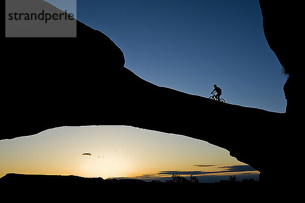 Ein Mountainbiker fährt über einen natürlichen Felsbogen in der Wüste in der Nähe von Moab  Utah.