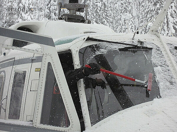 Ein Heliski-Pilot reinigt sein Fenster vom Schnee.