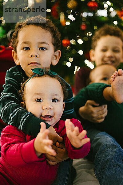Kleinkind hält kleine Schwester  während sie zu Weihnachten mit Geschwistern lächelt