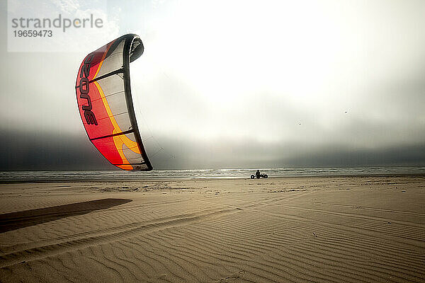 Silhouette eines männlichen Drachenbuggys (Drachenbuggy)  der in bedrohlichen Wolken und ungewöhnlichem Licht den Strand hinunterrollt.