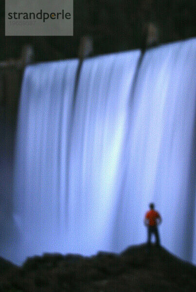 Ein Mann steht am Fuß des Clementine-Staudamms  als das Wasser die Spitze durchbricht und an ihm vorbeiströmt. Auburn  Kalifornien. (Weicher Fokus)