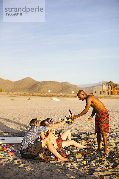 Eine Gruppe Erwachsener hängt am Strand und genießt den Sonnenuntergang und ein paar kühle Biere.