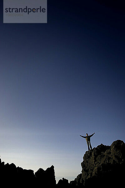 Ein Mann mit seinen Armen in einem „V“ auf Felsen in Oregon.