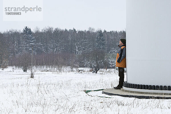Ein Mann lehnt auf dem Sockel einer Windkraftanlage auf seinem Bauernhof in der Nähe von Kobylnica  Polen.