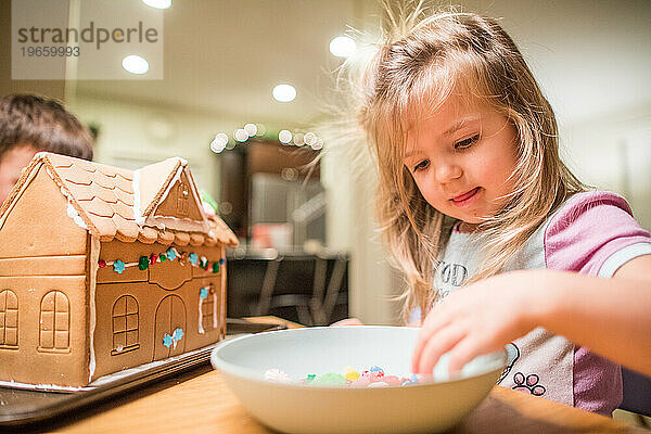 Süßes junges blondes Mädchen dekoriert ihr Lebkuchenhaus.