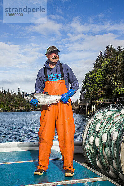 Porträt eines Mannes mit einem Lachs auf einem Boot in der kleinen Gemeinde Halibut Cove  Alaska.