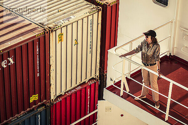 Eine ältere Reisende blickt von einem der Wohndecks eines Containerschiffs auf See auf das Meer.