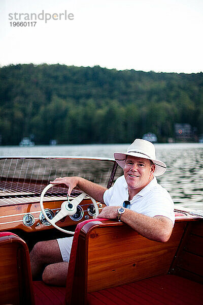 Ein Mann mit Bootshut fährt in der Abenddämmerung ein antikes Holzboot auf einem südlichen See.