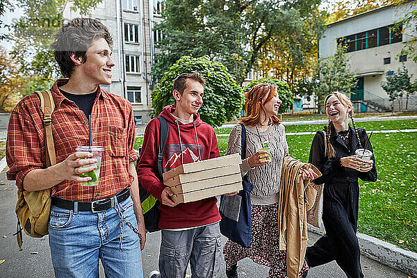 Fröhliche junge Leute  die mit Pizza und Getränken auf der Straße spazieren
