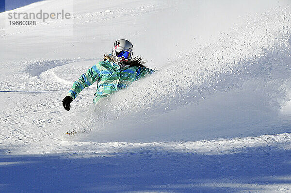 Eine Frau beim Snowboarden an einem Bluebird-Powder-Tag in einem Bergresort in der Nähe von South Lake Tahoe  Kalifornien.