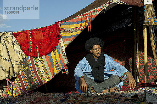 Ein Wüstenführer in traditioneller Kleidung in einem Zeltlager mit bunten Decken.