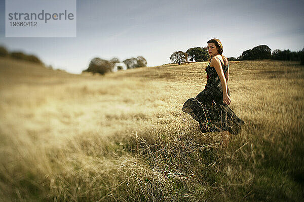 Eine Frau  die auf einem trockenen Feld spaziert  blickt zurück  Nordkalifornien. (Selektiver Fokus)