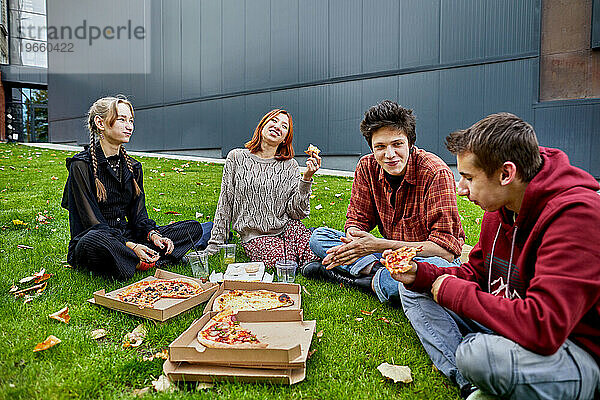 Gruppe von Freunden  die Pizza essen und auf dem Rasen lachen