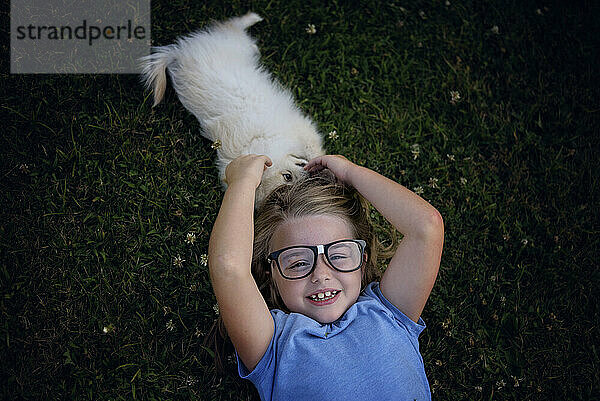 Kleines Mädchen mit Brille spielt mit weißem Spitz